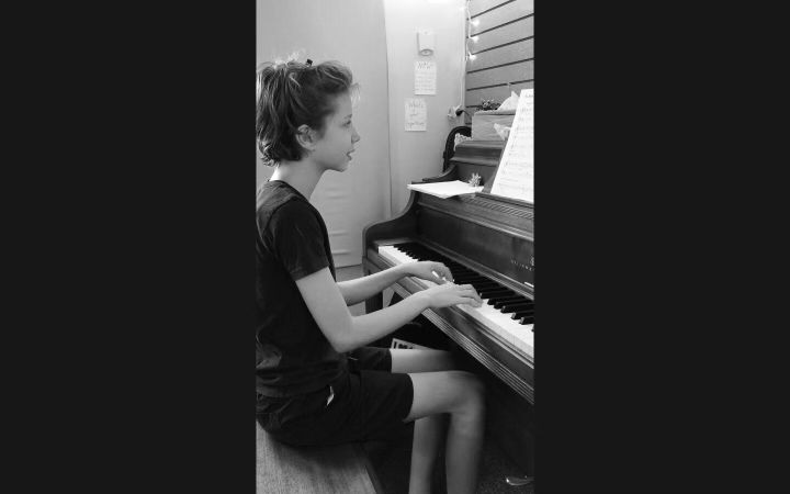 middle school kid playing piano with round hands and singing at the same time in a piano plus voice lesson