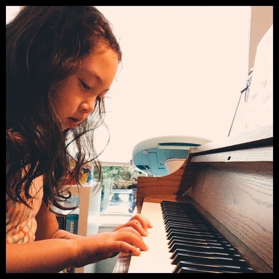 young child with long curly hair sitting at the piano carefully looking at her fingers on the keys during her piano lesson