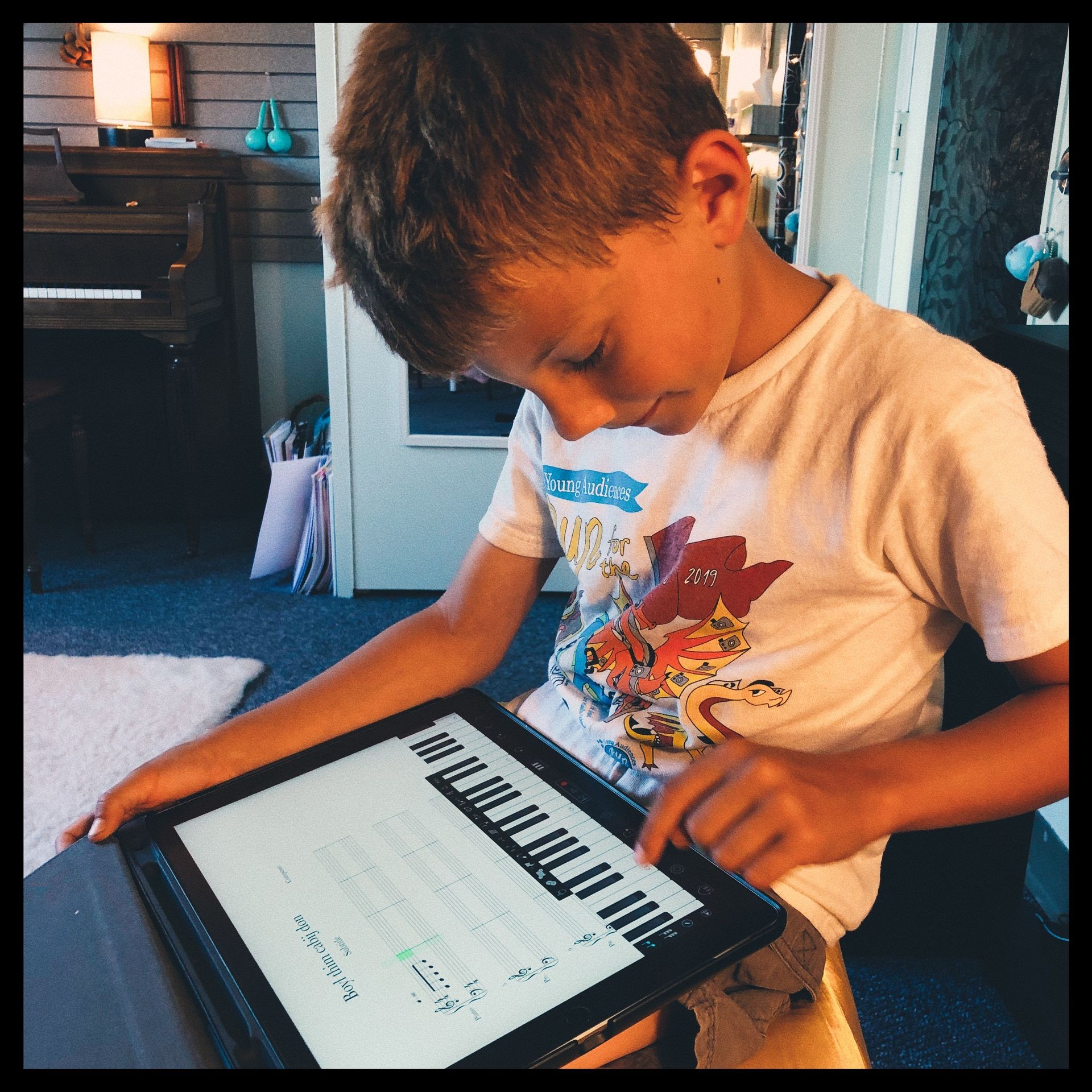 young child with short hair tapping a piano keyboard on an ipad during a piano and composition lesson