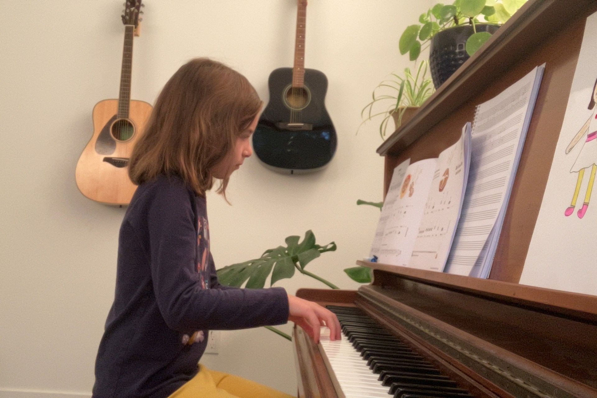 child playing piano during piano lesson, looking very focused and ready leaning in a bit with very round hands on the keys and guitars in the background