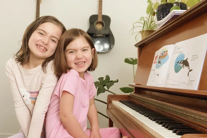 Two sisters smile together at the piano
