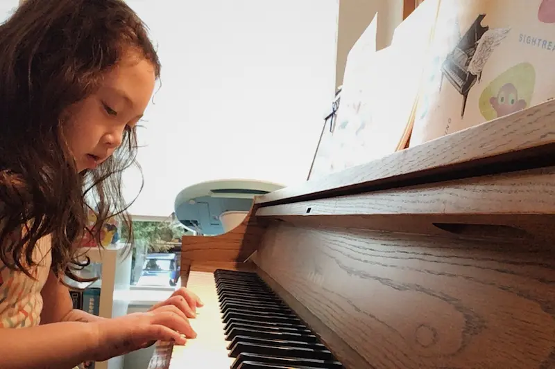 Child looks at her hands while playing piano during an online piano lesson