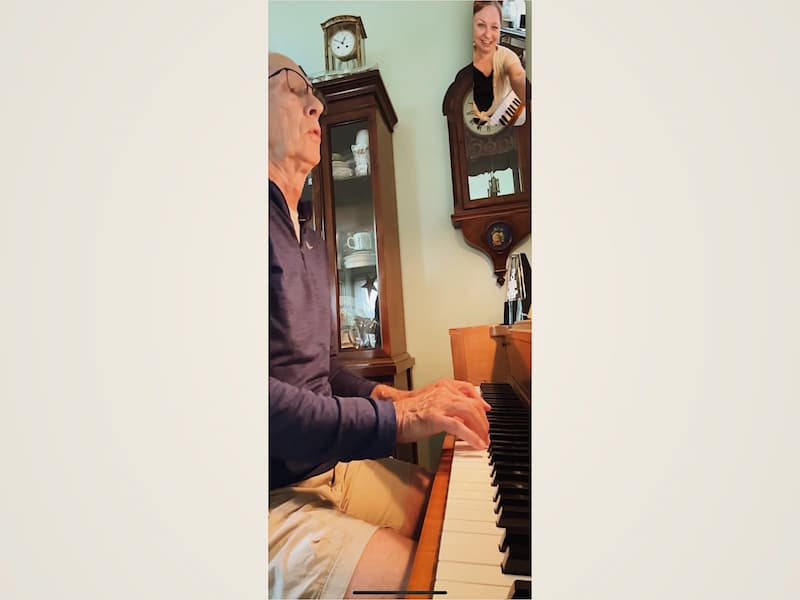An older learner plays piano during an online lesson