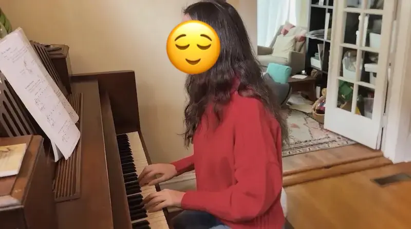 A teen student reads her sheet music as she plays piano during an online piano lesson