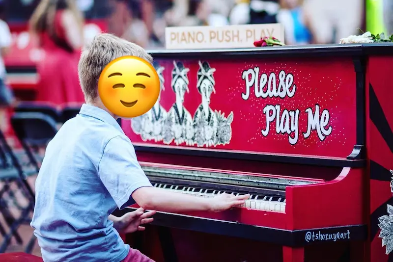 Blonde boy in light blue collared shirt playing a red piano